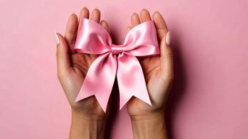 Woman holding pink bow in open hands on pink background with place for text video