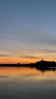 Tranquil sunset over lake with wind turbine and reflected colors in calm waters video