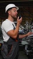 Industrial worker programmer sets up production line conveyor and gives commands via radio walkie talkie video