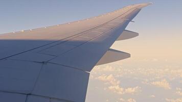view from the airplane window to the wing and clouds at sunrise, blue sky video