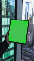 Man holding a tablet with green screen in a window in a city photo