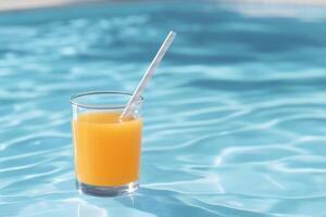 A refreshing glass of orange juice with a straw floats in a pool. photo