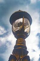 A close up view of an old, weathered street lamp against a cloudy sky. The lamp's rustic design and patina give it a vintage charm, making it an interesting subject for photography photo