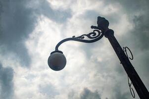 A vintage street lamp with ornate metalwork stands against a dramatic cloudy sky, creating a nostalgic and moody atmosphere photo