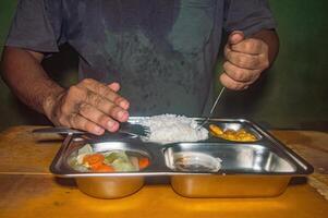 A person is eating a nutritious meal consisting of rice, vegetables, and fried food from a stainless steel tray, emphasizing the concept of a healthy and free lunch photo
