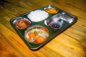 A nutritious and healthy free lunch concept featuring rice, vegetables, fried plantains, and a side of sauce, served on a stainless steel tray photo