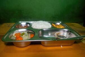 A stainless steel tray with a nutritious meal consisting of rice, vegetables, meat, and a small container of sauce, representing a healthy and balanced free lunch concept photo