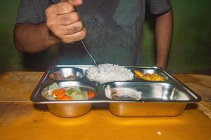 A person is having a nutritious and healthy free lunch consisting of rice, vegetables, and fried items on a stainless steel tray. The meal is balanced and visually appealing photo