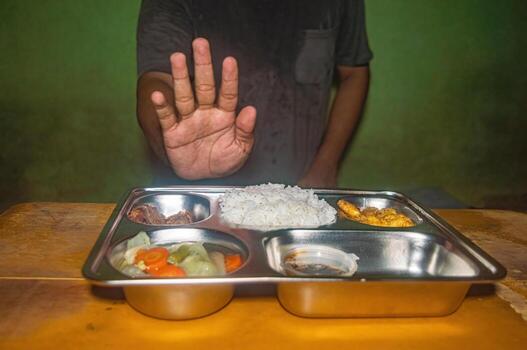 A person is refusing a meal by raising a hand in front of a tray containing rice, vegetables, and fried food. This image represents the concept of free lunch or healthy eating photo