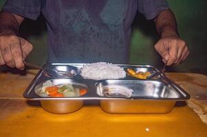 A person is having a nutritious and healthy free lunch consisting of rice, vegetables, and a side dish on a stainless steel tray, showcasing a balanced meal photo