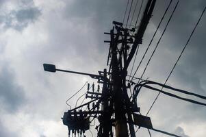 A silhouette of a utility pole with numerous wires and a streetlight against a cloudy sky, highlighting urban infrastructure photo