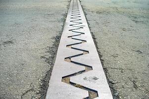 Close up of a bridge expansion joint with a zigzag pattern, designed to accommodate structural movements and prevent damage photo