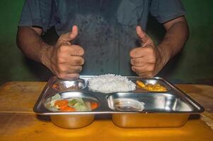 A person gives two thumbs up in front of a stainless steel tray filled with a nutritious meal, including rice, vegetables, and side dishes, symbolizing a healthy and free lunch concept photo