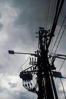 silhouette of a utility pole with numerous wires and a streetlight against a cloudy sky, highlighting urban infrastructure photo
