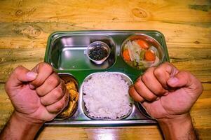 A stainless steel lunch tray with rice, fried chicken, vegetables, and sauce, held by hands with a fork and spoon crossed over the rice, symbolizing a nutritious free lunch photo