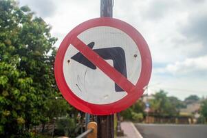 A close up of a No Left Turn traffic sign with a red circle and diagonal line over a black left arrow, set against a blurred background of trees and a road photo