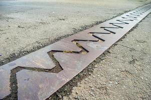 close up view of a bridge expansion joint with a zigzag pattern, designed to accommodate structural movements and prevent damage. The metal plate is embedded in the asphalt road surface photo