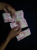 Hands holding stacks of one hundred thousand Indonesian Rupiah banknotes against black background photo