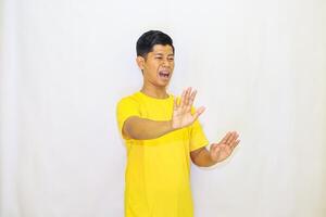 A man in a yellow shirt expresses disgust and rejection with raised hands against a white background, showing an obvious dislike for something, photo