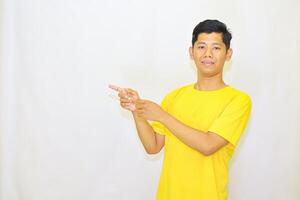 Young man in a yellow t-shirt with a warm smile, pointing towards the left with a focused gaze, showcasing a gesture for announcements or directions, photo