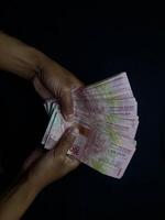 Hands holding a stack of Indonesian Rupiah banknotes against a dark backdrop photo