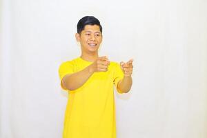 Young Man in Yellow Shirt Points Forward with Both Hands, Expressing Enthusiasm or Selection, Against a Plain White Backdrop photo