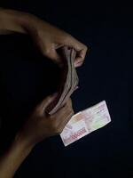 Close up of hands holding and counting Indonesian Rupiah money against a black background photo