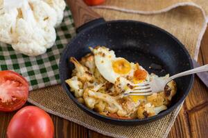 omelette with cauliflower and vegetables in a frying pan on a wooden table photo