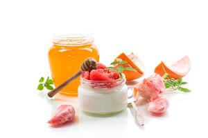 Perfect breakfast. homemade sweet yogurt in a glass jar with pieces of red ripe grapefruit and honey, isolated on white background photo