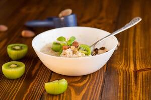oatmeal with kiwi, honey and nuts in a bowl on a wooden table photo