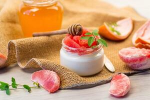 Breakfast, homemade sweet yogurt in a glass jar with pieces of red ripe grapefruit and honey, on a wooden table photo