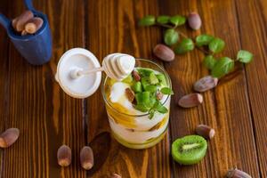 Breakfast, homemade yogurt with kiwi, honey and nuts in a glass on a wooden table photo
