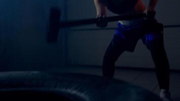Womna athlete in athletic form with powerful and strong blows beats on the tire with a hammer does a crossfit exercise video
