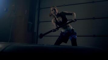 The woman performs an intense exercise, delivering powerful hammer blows to the tire with a hammer video