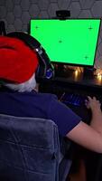 Rear view of teenage in a red Santa hat uses a computer, sits in front of a green monitor video