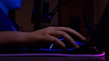 fechar acima do adolescente mão usa uma computador rato com néon iluminação, inferior visualizar, dentro uma Sombrio quarto video