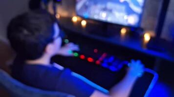 A blurry view of some teenager sitting at a dark desk and using a computer with a neon-lit keyboard video