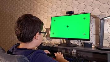A teenager uses a computer with a green screen monitor while sitting at a dark computer desk video