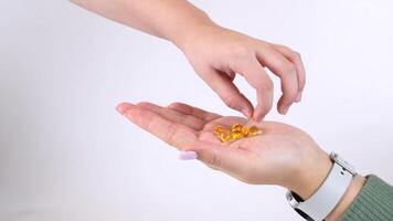 Hand releasing golden capsules into another hand in sequence video