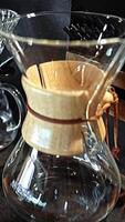 Glass coffee carafes chemex, with paper filter, ancient artisanal brewing in transparent vesseles, with help of pour-over method, craftsmanship in coffee-making, close-up, rustic ambiance, vertical. video