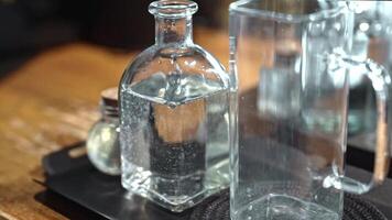 Glass bottle with sparkling water standing near empty glass on wooden table in warm light, minimalist drink setup symbolizing clarity and purity, focus on clean design and transparent textures. video
