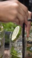 Bartender puts straw in glass,, hand cooking cocktail with lime and mint, close-up of refreshing drink preparation, fresh ingredients in clear glass, symbol of summer, cooling refreshment, vertical. video