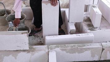 A skilled construction worker is using specialized equipment to apply adhesive cement paste for lightweight bricks to build a strong wall in a construction site. video