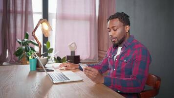 african businessman ordering and paying on website of internet-shop, sitting at table with laptop video