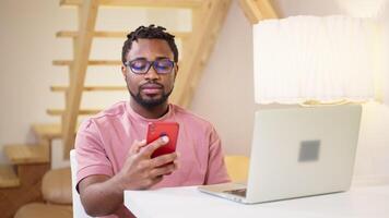 black man checking email and messengers in smartphone when working at home, portrait of african guy video