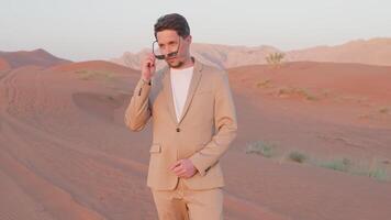 Tourist businessman puts on sunglasses stands in sand dunes red desert in UAE. video