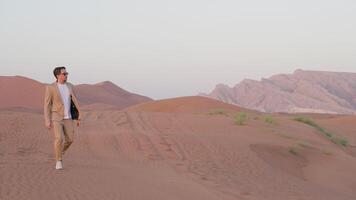 lonely man walking in empty lifeless desert, strolling on sand dunes in sunset, full-length portrait video