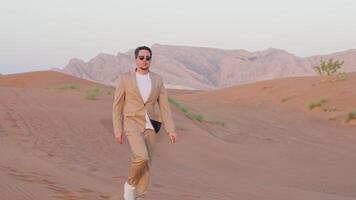 Successful stylish businessman in suit sunglasses walking in red desert in UAE. video