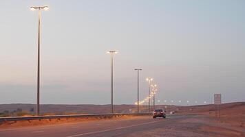 Road illuminated by lanterns with moving car in desert at dusk in evening. video