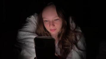 Teen girl lying in bed at night using smartphone, scrolling social media and texting. Not healthy sleep. Insomnia and the harm of the smartphone before going to bed. Dependence on social networks video